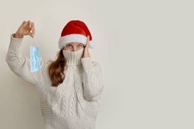 Noel Baba şapkalı kadın yüzünü yaka takmış ve koruyucu maske takmış.