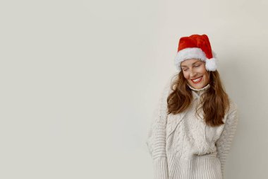 Kazak giyen ve Noel Baba şapkalı bir kadın aşağıya bakıp gülümsüyor.