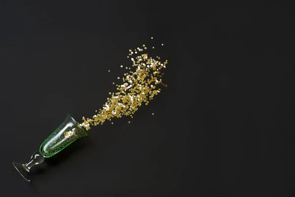 A spilled glass with golden glitter on black background — Stock Photo, Image