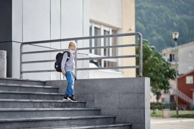 Yüzü maskeli çocuk okuldan çıkıyor.
