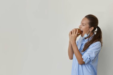 Maskeli güzel bir kadın vejetaryen burger manzarası yiyor.