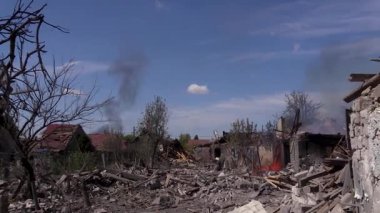 Destroyed houses, burnt trees in the village after shelling, fire can be seen on the site of the former house. One of the houses on the street burns out. Villages and cities were destroyed during