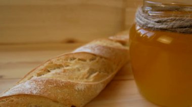 Masanın üzerinde bir kavanoz altın bal, bir baget ve tahta kaşığın yanında. Tatlı, sağlıklı bir tatlı gibi