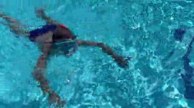 8-9 yaşındaki bir çocuk havuzda maskeyle yüzüyor, dalıyor ve yüzüyor. Havuz kenarında dinleniyorum..