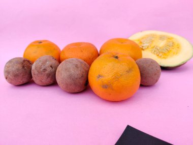 Portakal gibi meyveler, sapodilla / chikoo ve pembe arka planda yarım dilimlenmiş balkabağı..