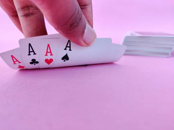 South Indian man raises playing cards to see his cards which contains Four aces. Pink background