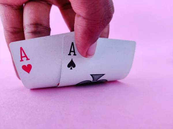 South Indian man raises playing cards to see his cards which contains Two ace. Pink background