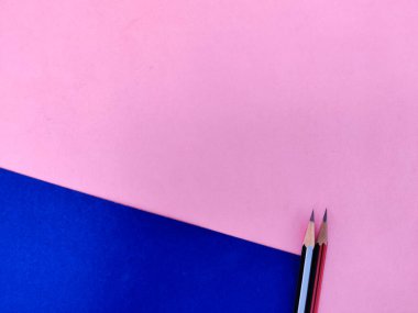 Pembe ve mavi arkaplanda izole edilmiş siyah ve kırmızı renkli iki keskin kalemin boşluğunu kopyala