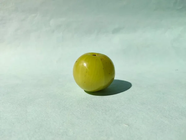 One Indian gooseberry or amla with shadow isolated on green background