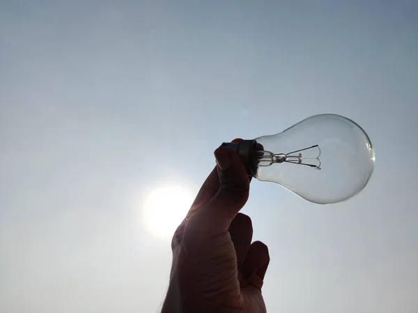 South Indian young man holding one light bulb in horizontal position with sunny sky background