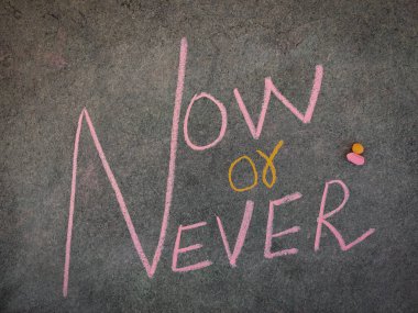 Gri tahtadaki yazı, ya şimdi ya da asla. Renkli tebeşir parçaları kullanılıyor.