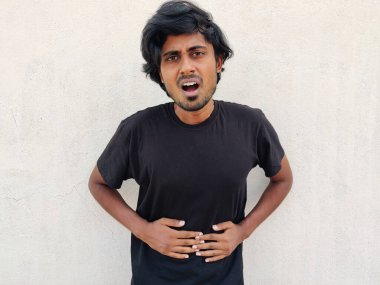 Mide ağrısı ya da mide rahatsızlığı çeken siyah tişört giyen genç bir Güney Hintli. Beyaz arkaplan