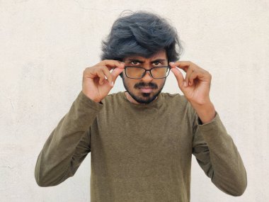 Kızgın Güney Hintli genç adam gözlük takıyor. Ciddi gözler. Bir şeye kızmış gibi görünüyor. Beyaz arkaplan.