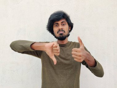 Yeşil renkli, uzun kollu, yakışıklı genç adam iyiye işaret ediyor. Baş parmaklar yukarı ve baş parmaklar aşağı. Beyaz arkaplan