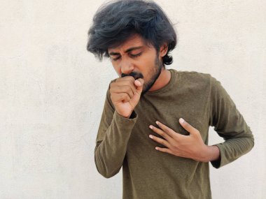 Genç yakışıklı adam yumruğuna öksürüyor. Ciğerlerde sorun var gibi. Covid 19 konsepti. Beyaz arkaplan