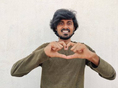 Yeşil kolları olan yakışıklı bir adam. Sevgiyle gülümsüyor. Elleriyle kalp sembolü yapıyor..