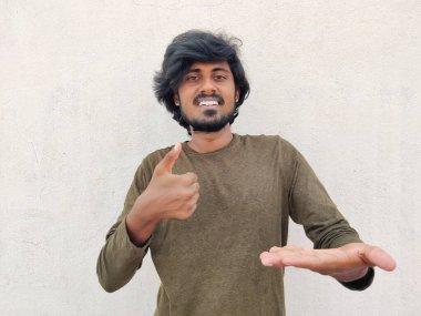 Gülümseyen yakışıklı adam bir elinde sanki sanal ve görünmez bir şey gösteriyormuş gibi baş parmağını kaldırıyor. Beyaz arkaplan