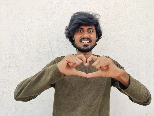 Yeşil kolları olan yakışıklı bir adam. Sevgiyle gülümsüyor. Elleriyle kalp sembolü yapıyor..