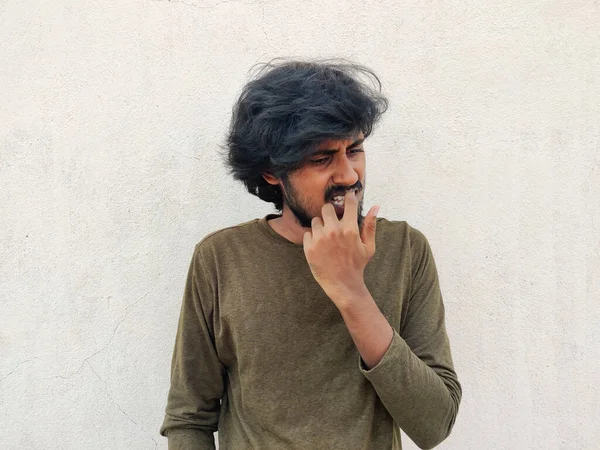 Uzun saçlı genç Güney Hindistanlı adam sol el tırnaklarını yiyor. Hüsran modu. Beyaz arkaplan