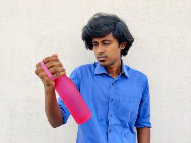 20 'li yaşlarda yakışıklı bir adam pembe renkli bir su şişesi tutuyor ve onu görüyor. Beyaz arkaplan