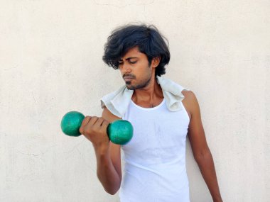 Beyaz spor elbiseli zayıf Hintli adam dambıllarla pazı egzersizi yapıyor.