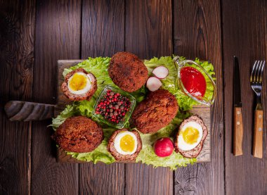 İskoç yumurtası. Kıymaya sarılmış yumurta sarısı ve kaynamış yumurta. Ağaç tepsisinde baharatlı yeşille servis edilmiş, yukarıdan manzaralı. Düz yatıyordu