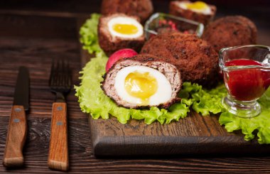 İskoç yumurtası. Kıymaya sarılmış yumurta sarısı ve kaynamış yumurta. Ağaç tepsisinde baharatlı yeşille servis edilmiş, yukarıdan manzaralı. Düz yatıyordu