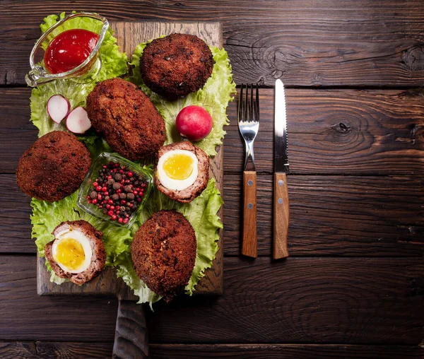 Scotch eggs. Soft boiled eggs with runny yolk wrapped in minced meat. Served with spiced green on a wood tray, view from above. Flat lay