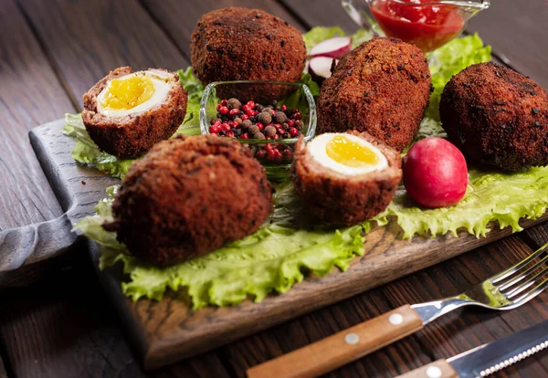 Scotch eggs. Soft boiled eggs with runny yolk wrapped in minced meat. Served with spiced green on a wood tray, view from above. Flat lay