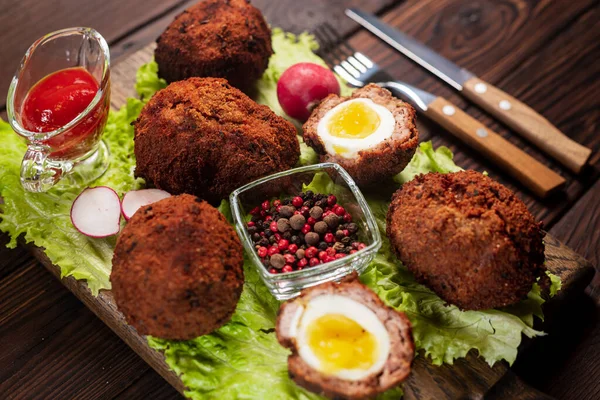 Scotch eggs. Soft boiled eggs with runny yolk wrapped in minced meat. Served with spiced green on a wood tray, view from above. Flat lay