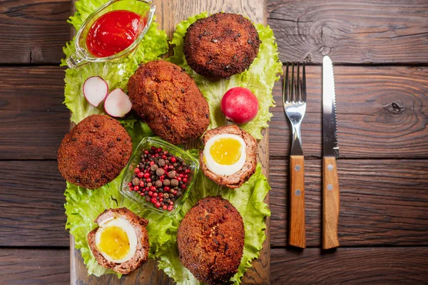 Scotch eggs. Soft boiled eggs with runny yolk wrapped in minced meat. Served with spiced green on a wood tray, view from above. Flat lay