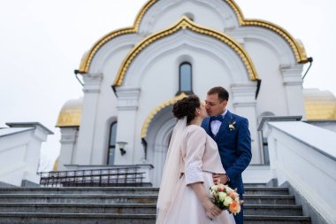 Gelin ve damat kilisenin arka planında, dini âşıklar, kışın düğün yürüyüşü, bir erkek ve bir kadın nazikçe öpüşüp gülümsüyor.
