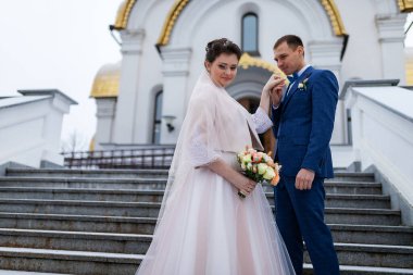 Gelin ve damat kilisenin arka planında, dini âşıklar, kışın düğün yürüyüşü, bir erkek ve bir kadın nazikçe öpüşüp gülümsüyor.