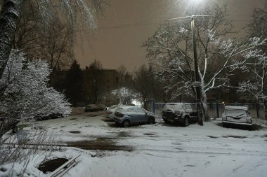 Sokak lambalarının ışığı altında, park yerindeki arabalar karla kaplıydı, araba sahipleri için şiddetli kar fırtınası, şehirde kış yağışı nedeniyle sorunlar vardı.