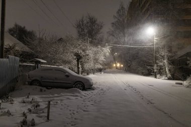 Sokak lambalarının ışığı altında, park yerindeki arabalar karla kaplıydı, araba sahipleri için şiddetli kar fırtınası, şehirde kış yağışı nedeniyle sorunlar vardı.