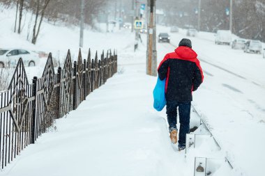 Zorlukla yürüyen bir adam, yoğun bir kar yağışı sonrası kaldırımda kar yağışı yapar. Kışın kamu hizmetlerinin kötü işleyişi
