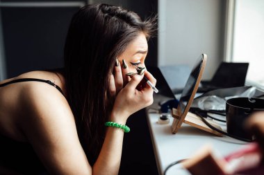Bir kız aynanın önünde gözlerine makyaj yapar, özel bir durum için makyaj yapar.