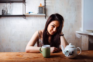 Kız evde kahvaltı yapıyor. Bardaktan sıcak kahve iç.