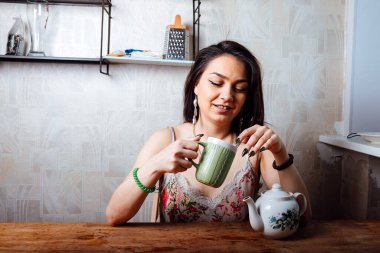 Kız evde kahvaltı yapıyor. Bardaktan sıcak kahve iç.