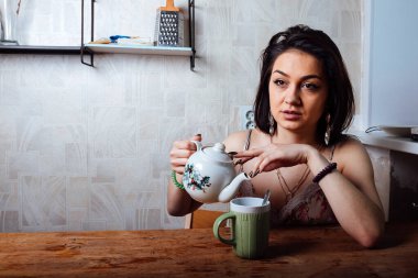 Kız evde kahvaltı yapıyor. Bardaktan sıcak kahve iç.