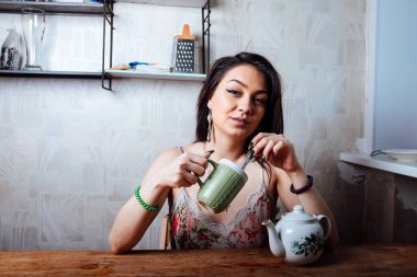 Kız evde kahvaltı yapıyor. Bardaktan sıcak kahve iç.