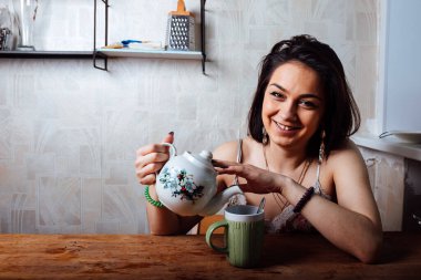 Ev elbiseli bir kız masada oturuyor. Hafif bir kahvaltı var. Bir fincana sıcak çay dök.
