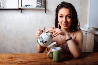 Ev elbiseli bir kız masada oturuyor. Hafif bir kahvaltı var. Bir fincana sıcak çay dök.