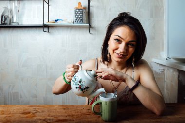 Ev elbiseli bir kız masada oturuyor. Hafif bir kahvaltı var. Bir fincana sıcak çay dök.