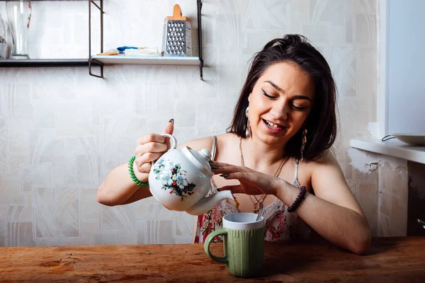 Ev elbiseli bir kız masada oturuyor. Hafif bir kahvaltı var. Bir fincana sıcak çay dök.