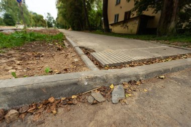 Yol boyunca kırık kaldırım. Kaldırımın tamiri. Çatlak beton döşemeler ve düşük kalite malzemeler. Yol işçilerinin yozlaşması