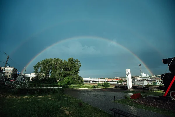 rainbow in the sky over the city after the rain. an old steam locomotive stands at the railway station