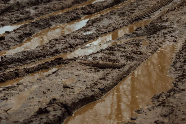 Çamurlu yolda çamur. Islak ve yumuşak zeminde geçen arabaların tekerleklerindeki izler. Yol, ulaşım için zordur. Toprak bir yolun çukurlarında su birikintileri