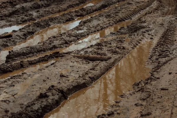 Çamurlu yolda çamur. Islak ve yumuşak zeminde geçen arabaların tekerleklerindeki izler. Yol, ulaşım için zordur. Toprak bir yolun çukurlarında su birikintileri