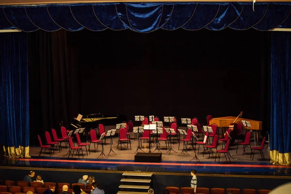 Sahneden boş konser salonunun manzarası. Sahnede müzisyenler için sandalyeler ve enstrümanlar var. Ünlü orkestranın performansı için filarmoni orkestrasının hazırlığı